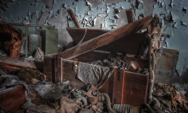 Wooden crate lies open, revealing scattered gas masks inside a dilapidated room with peeling paint and debris. A sense of abandonment permeates the space. No text is present.
