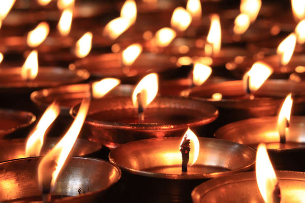 Numerous small candle flames flicker atop metal holders, casting warm, soft light across a crowded, dimly lit space, creating a serene and contemplative atmosphere.