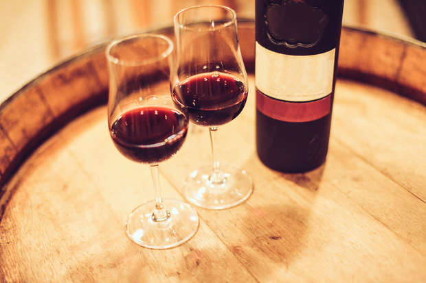 Two glasses of red wine and a bottle resting on a wooden barrel, creating a warm, inviting atmosphere with soft lighting.