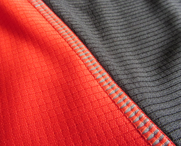 Red and black fabric panels with visible textured stitching, meeting at a seam. The stitch pattern creates a distinct line, highlighting the contrast between the vibrant red and dark black.