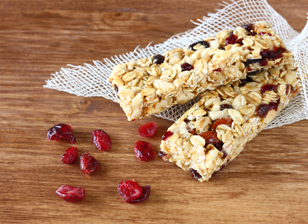 Granola bars embedded with oats and dried cranberries rest on a piece of white mesh, surrounded by scattered cranberries on a wooden surface.