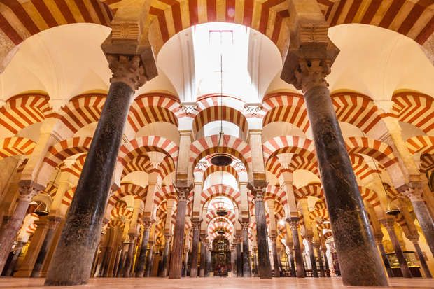 Ornate arches with red and white stripes rest on tall columns, creating a repetitive pattern in a grand, historic interior, evoking a sense of symmetry and architectural elegance.