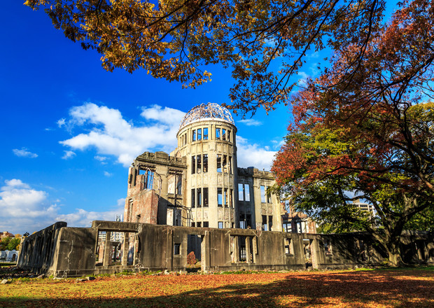 A ruined building, standing still, surrounded by autumn trees and a clear blue sky, with fallen leaves scattering the ground.