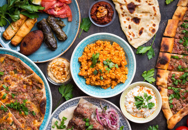 A variety of Middle Eastern dishes, including kebabs, flatbreads, rice, and dips, are arranged on a wooden table, garnished with fresh herbs for a vibrant and appetizing presentation.