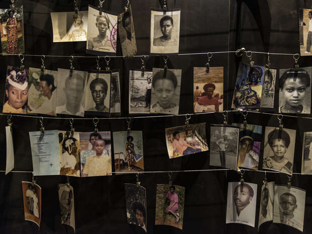 Various photographs hang on wires, depicting individuals in different settings. The dark background and minimal lighting suggest a solemn exhibition or memorial display, emphasizing remembrance and reflection.