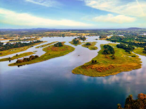 A serene river flows among lush green islands, creating winding waterways in a vast landscape under a clear blue sky.