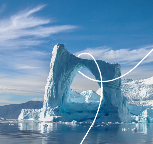A large iceberg with a natural arch appears in calm waters, under a clear blue sky with thin clouds, while snowy mountains are visible in the distant background.